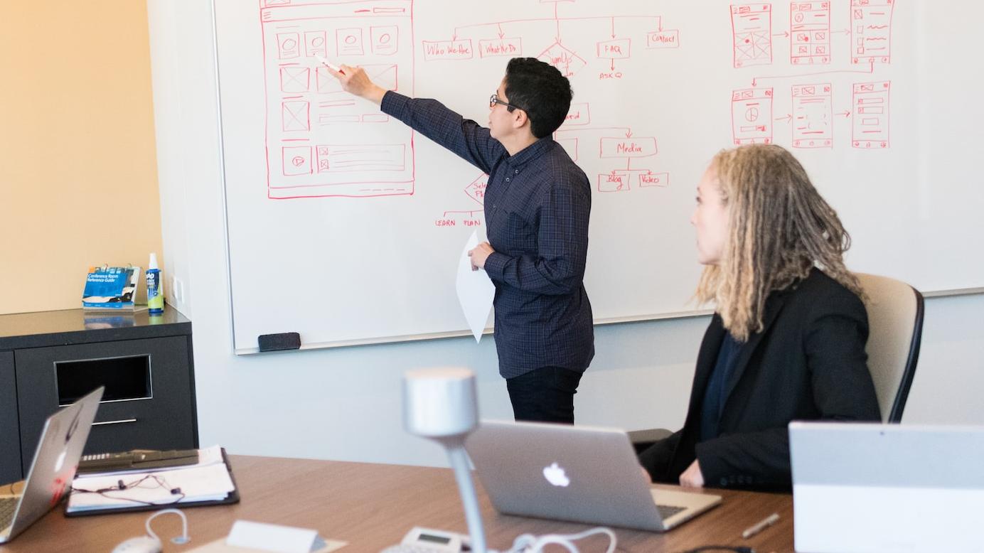 man in black dress shirt writing on dry-erase board